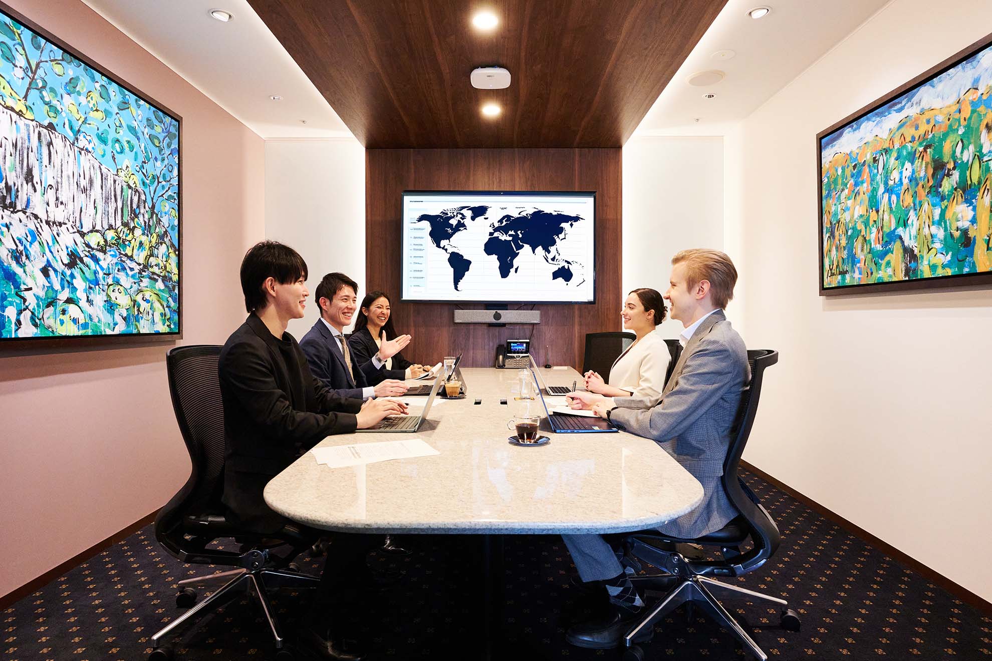 People seated around a conference table in a modern meeting room at Servcorp Twin 21 Mid Tower, with laptops open and a large world map displayed on a screen at the front of the room.