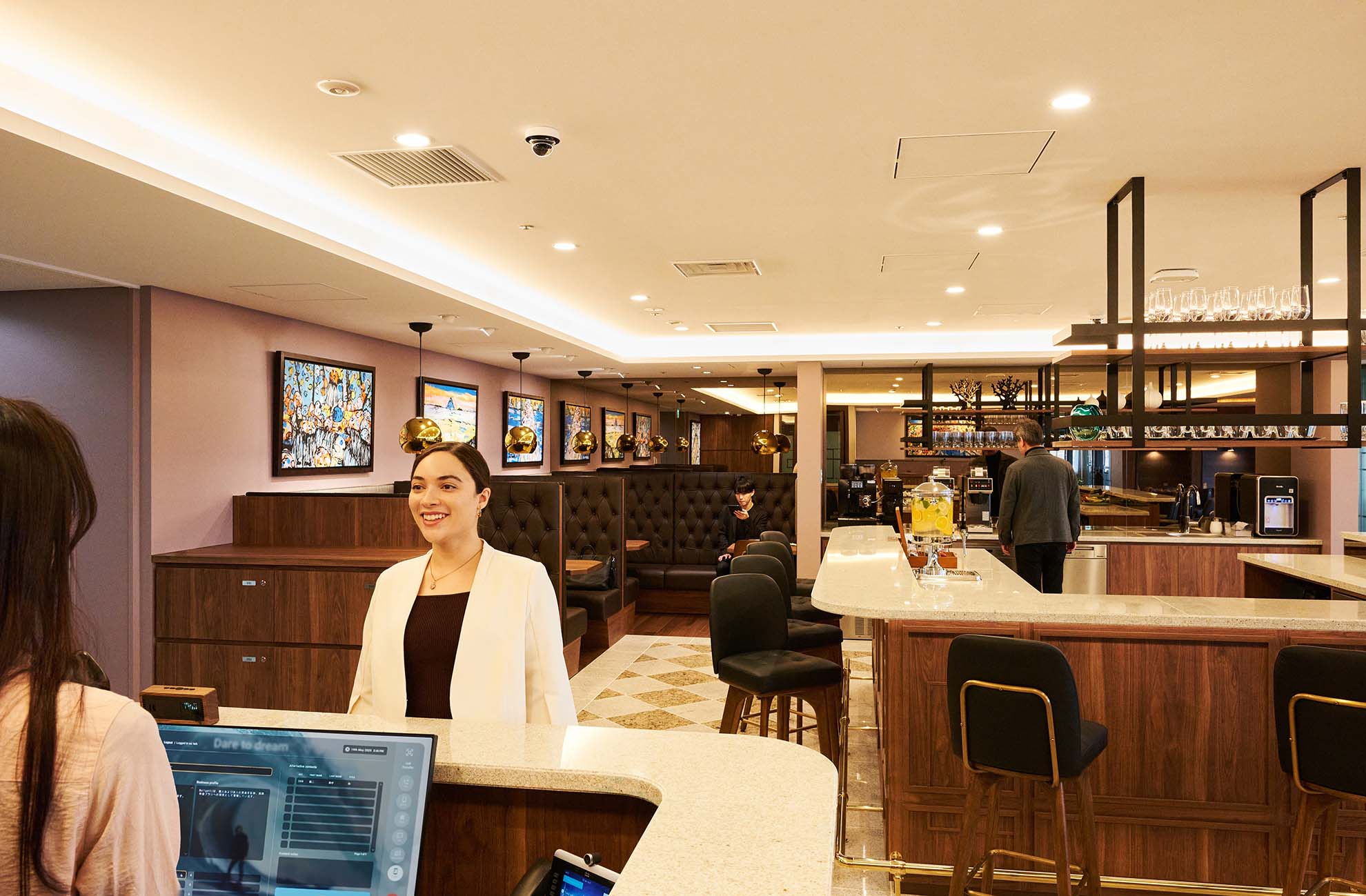 Reception and business lounge area at Servcorp Twin 21 Mid Tower, featuring a staffed front desk, bar‑style seating, and a modern interior with warm lighting and wood finishes.